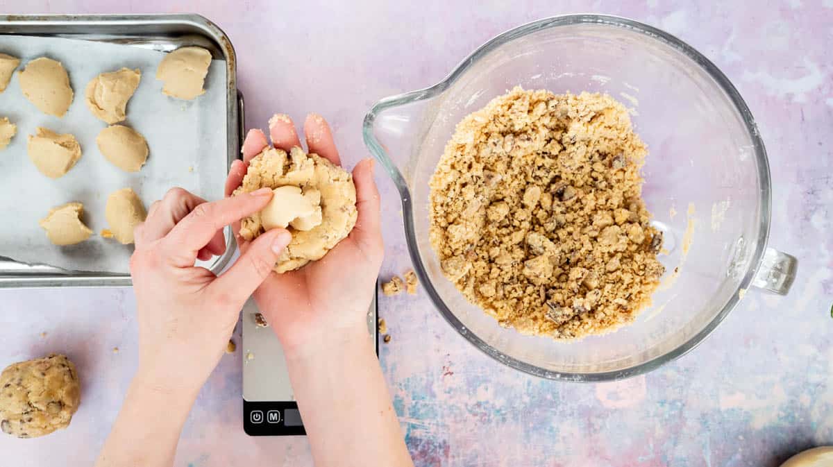A hand is placing a portion of Kinder-ella spread inside a portion of cookie dough.