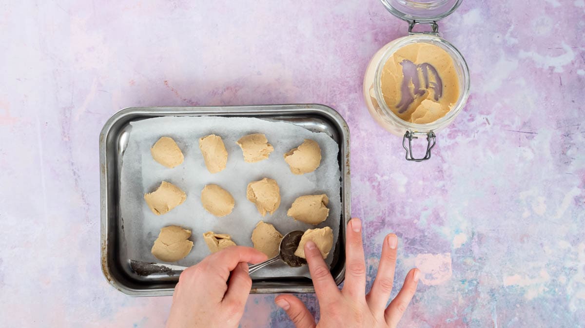 Two hands are using a spoon to prepare the Kinderella sauce for freezing in a lined baking tin.