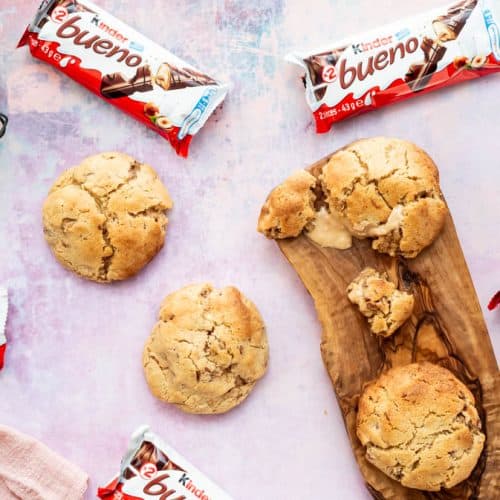 An overhead view of multiple Kinder Bueno cookies laid out and surrounded by Kinder Bueno bars. One cookie is broken open to reveal the molten middle.