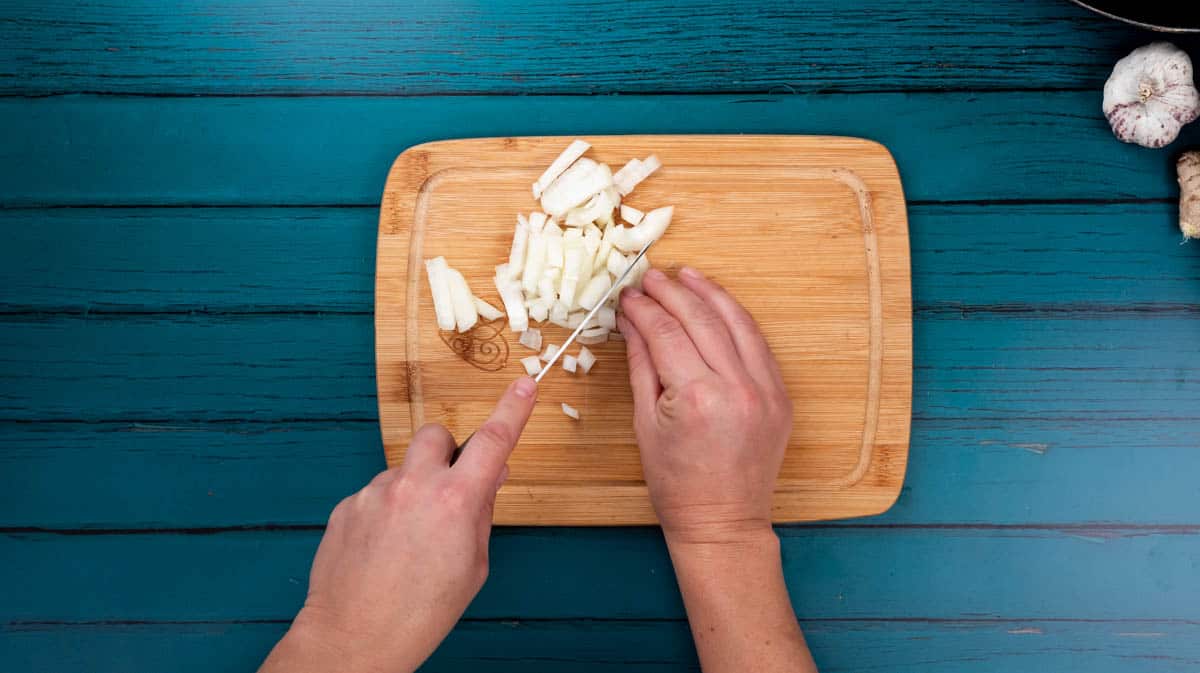 A person is using a sharp knife to roughly chop an onion on a chopping board.