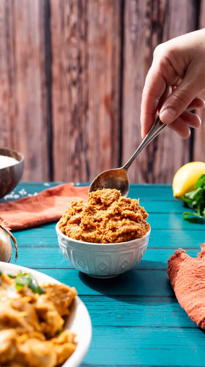 A person is using a spoon to scoop out some korma Curry paste from a small white bowl.