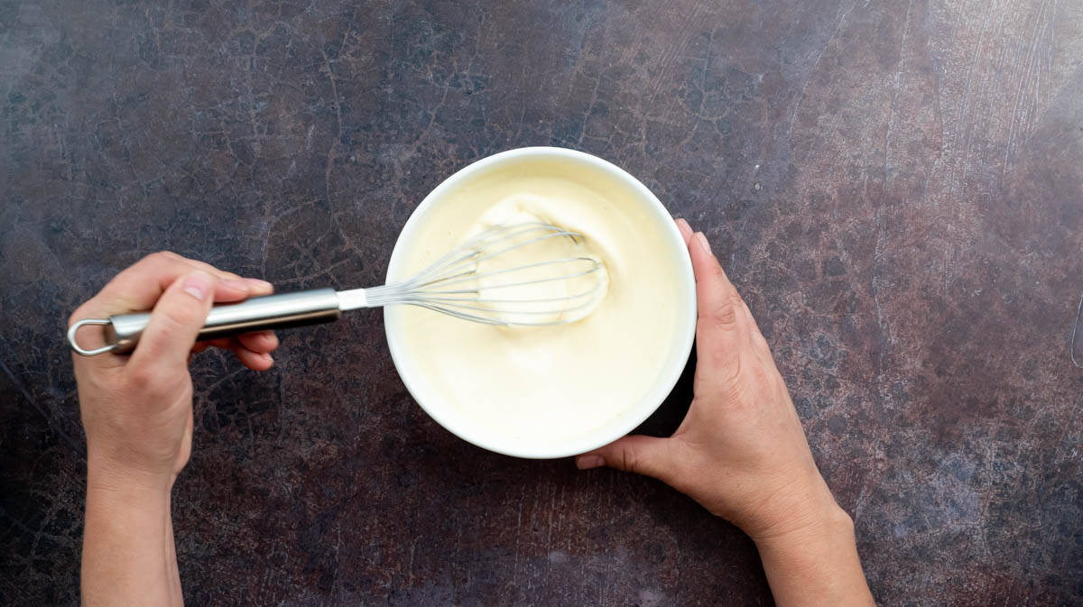 A hand is using a whisk to mix the double cream and egg together.