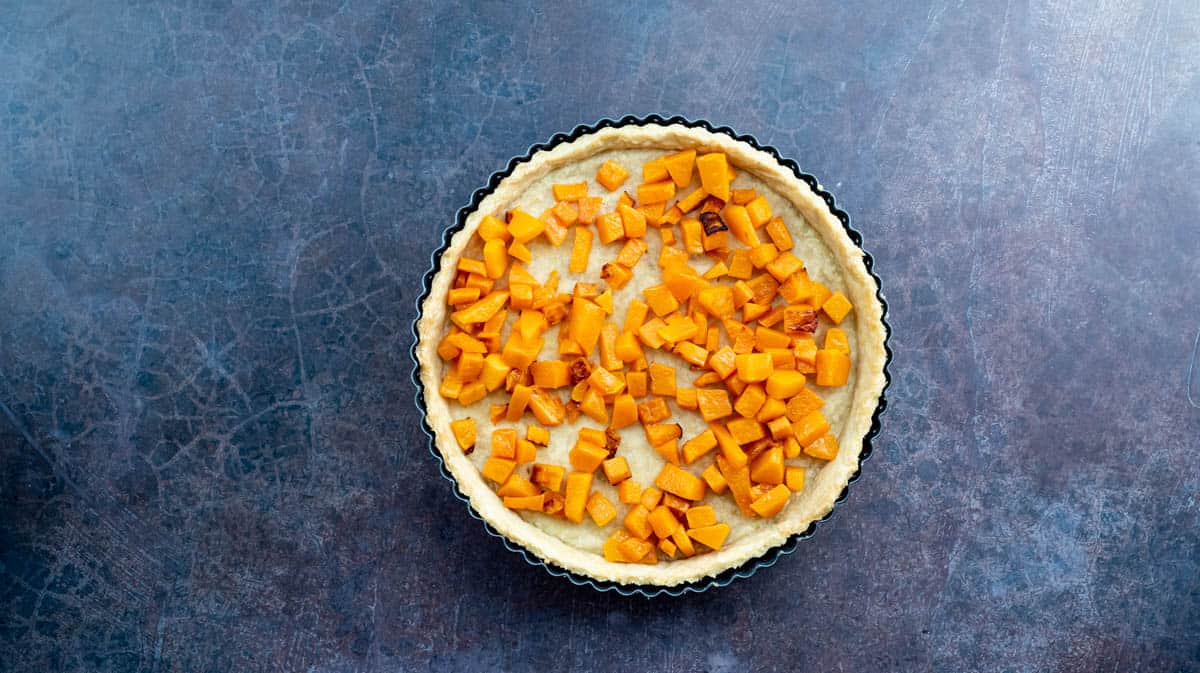 A photo of a part-baked pastry case that has been filled with roasted butternut squash cubes.