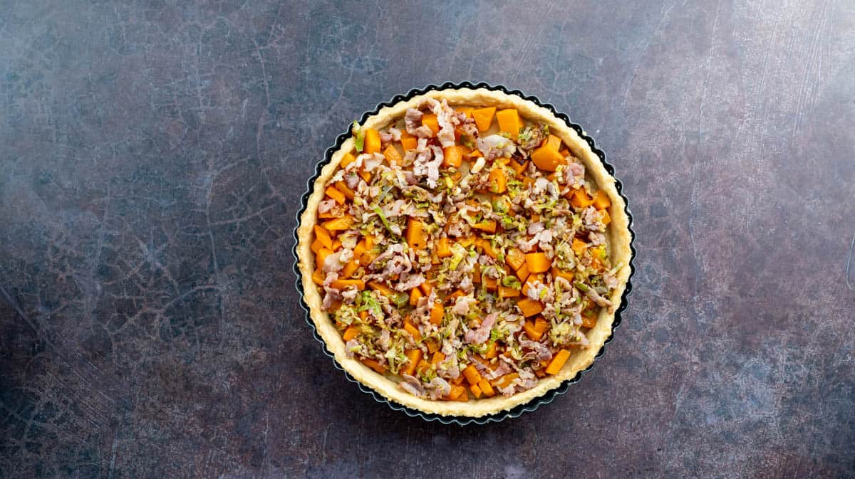 An overhead photo of a part-baked pastry case filled with butternut squash,. cooked leeks and bacon.