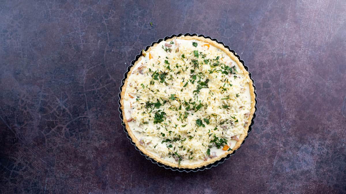 A photo of the prepared but unbaked leek and squash quiche that has been topped with fresh herbs, ready to go into the oven.