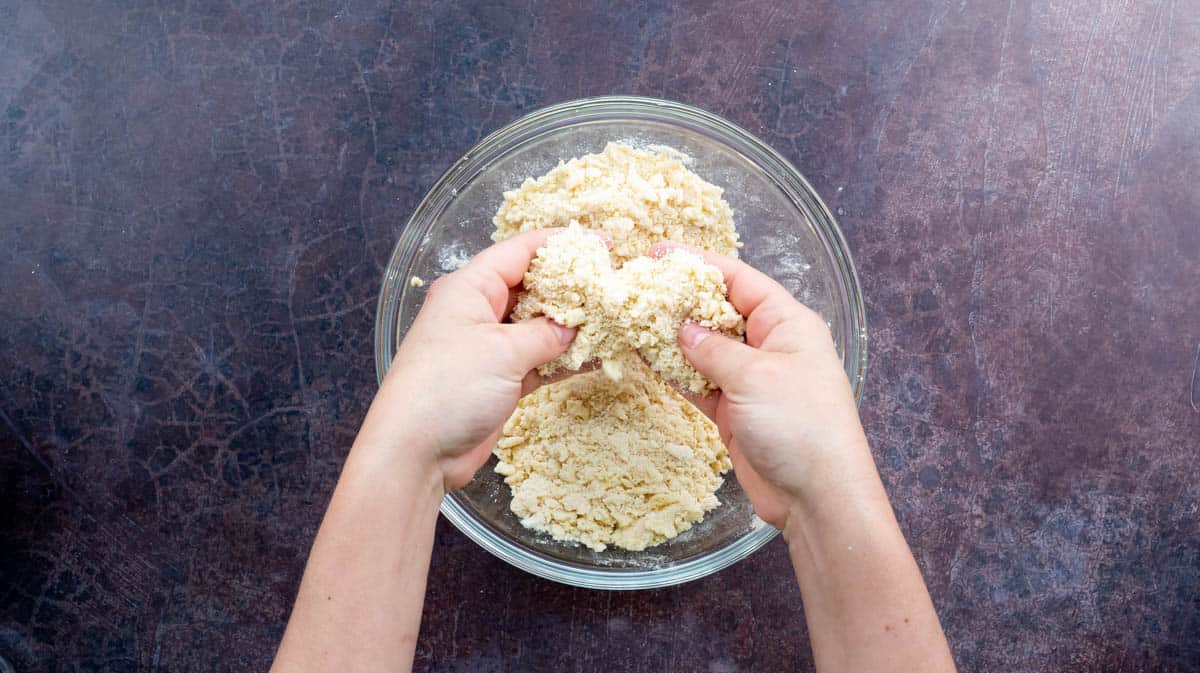Two hands are holding up the butter-flour mixture to show the breadcrumb texture.
