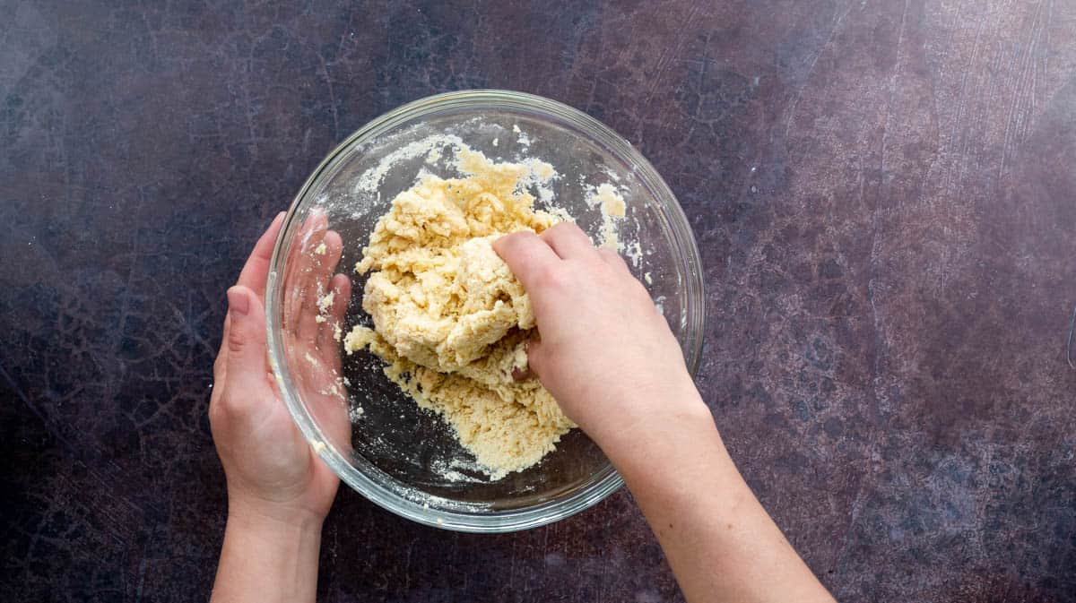 A hand is mixing the egg and water into the dry dough ingredients to create a dough.