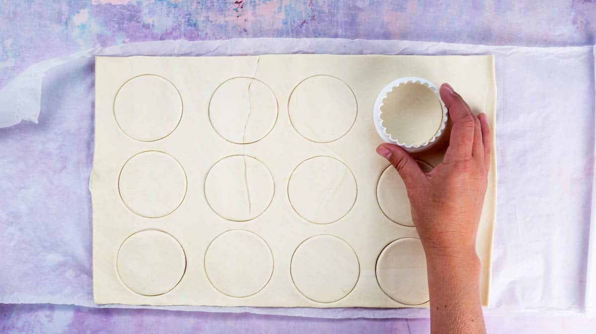 A hand is using a cookie cutter to cut out circles of puff pastry.