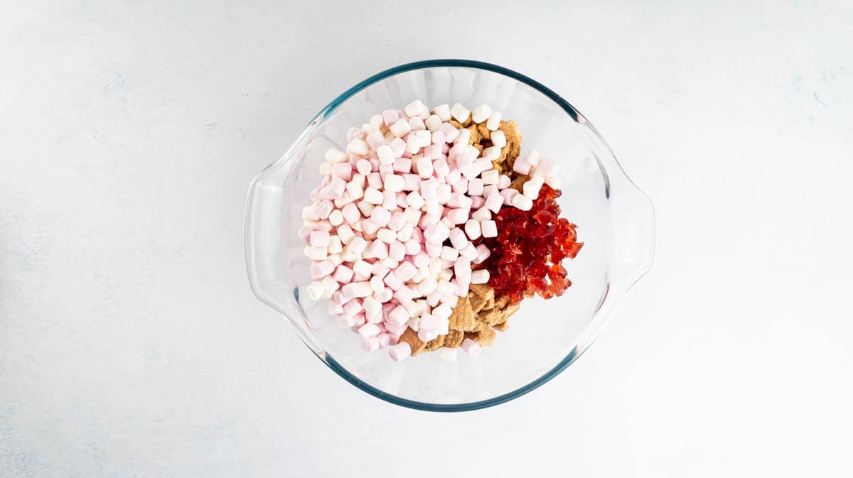 A glass bowl containing broken Malted Milk biscuits, marshmallows and glace cherries.