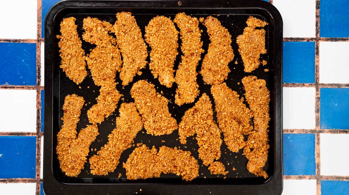 A baking tray filled with a single layer of uncooked Marmite chicken dippers.