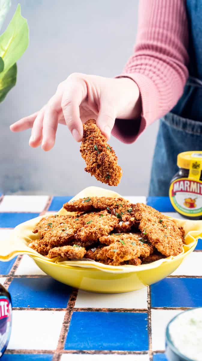 A person is lifting a Marmite chicken dipper from a bowl filled with them.