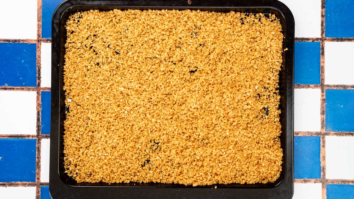 A large baking tray covered with a layer of untoasted Marmite bread crumbs.