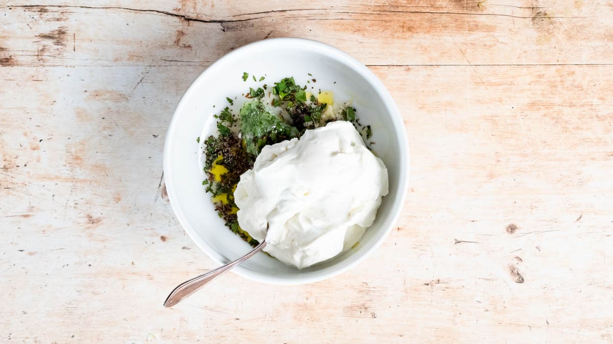 A white bowl filled with all the ingredients for the Raita sauce before being mixed together.
