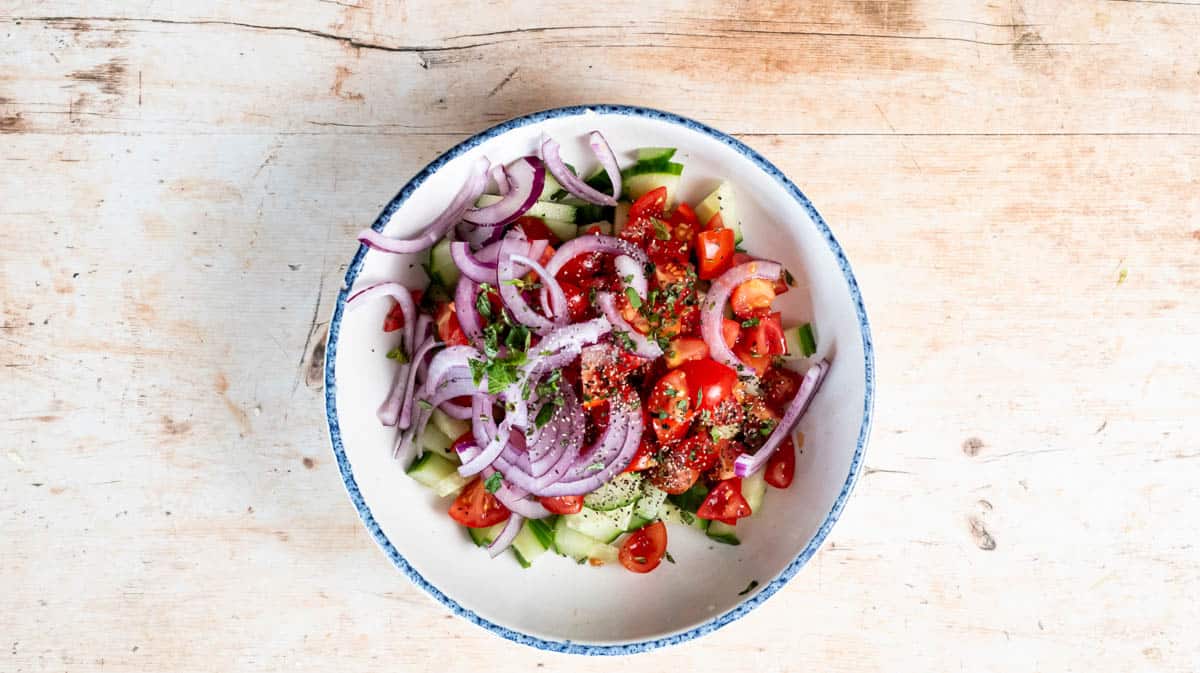 A bowl filled with Greek salad ingredients before being mixed together.