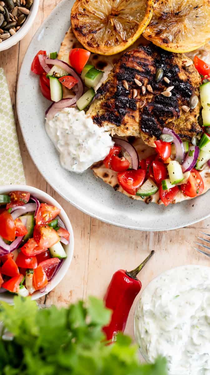 A plate with mint and coriander chicken on an open wrap, with salad and yoghurt dip. There is another bowl of salad and dip below the plate.