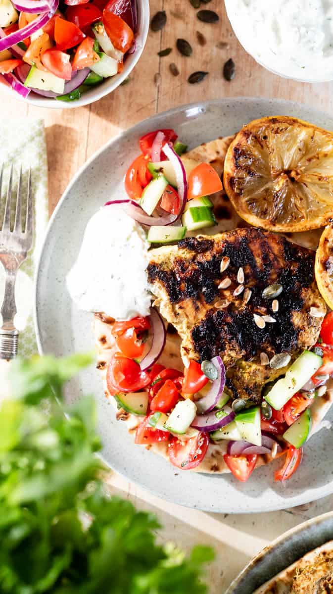 A plate filled with the open wrap ingredients, surrounded by bowls of salad, yoghurt dip, fresh coriander and seeds.