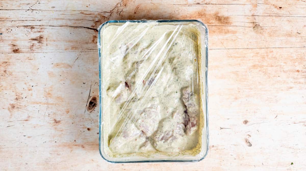 A glass dish filled with the marinated chick and covered in cling film.