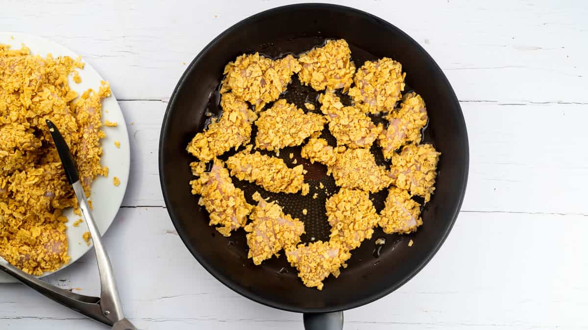A black frying pan filled with nacho chicken bites being shallow fried.