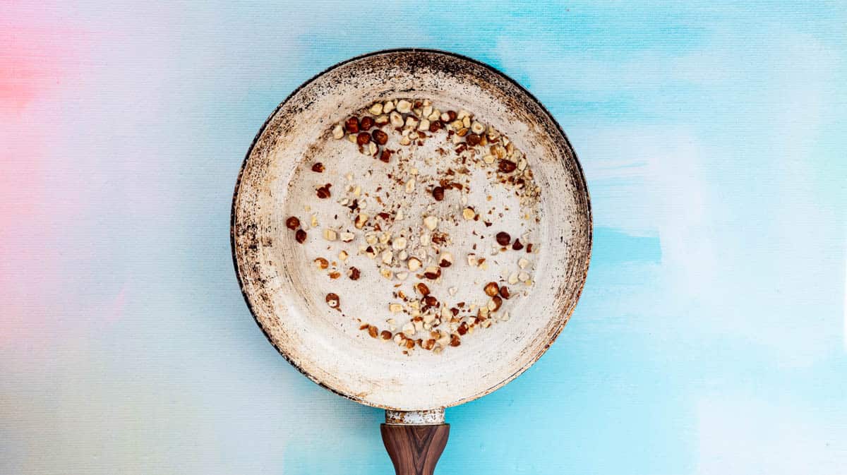 A frying pan with crushed hazelnuts inside.