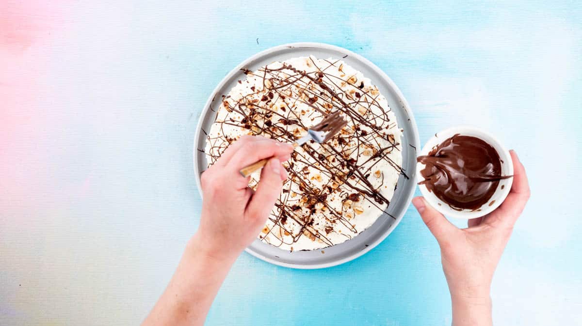 A hand is using a fork to drizzle melted Nutella over the top of the pie.