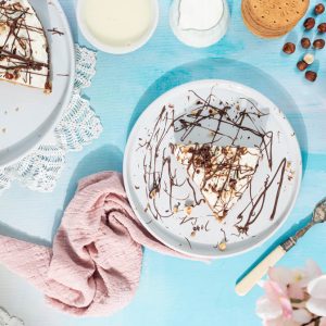 A slice of Nutella banoffee pie on a white plate next to a pink napkin, the rest of the cake is on a white plate to the left.