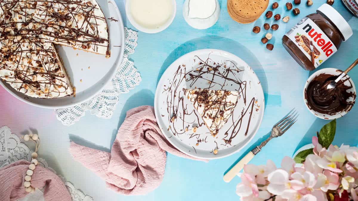 A slice of Nutella banoffee pie on a white plate next to a pink napkin, the rest of the cake is on a white plate to the left.