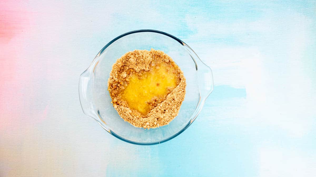 Crushed biscuit crumbs and melted butter inside a glass bowl.