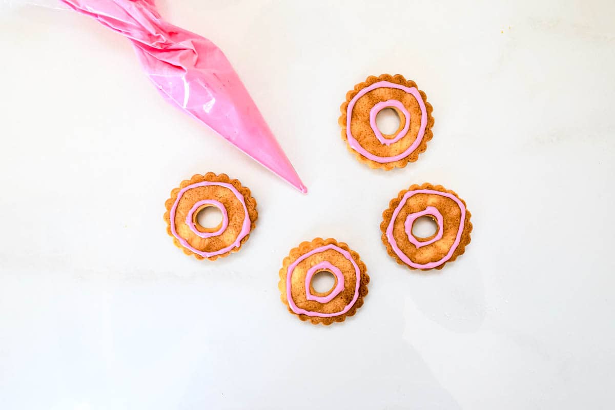 Four baked biscuits that have been lined with the initial step a flood and line icing in pink.
