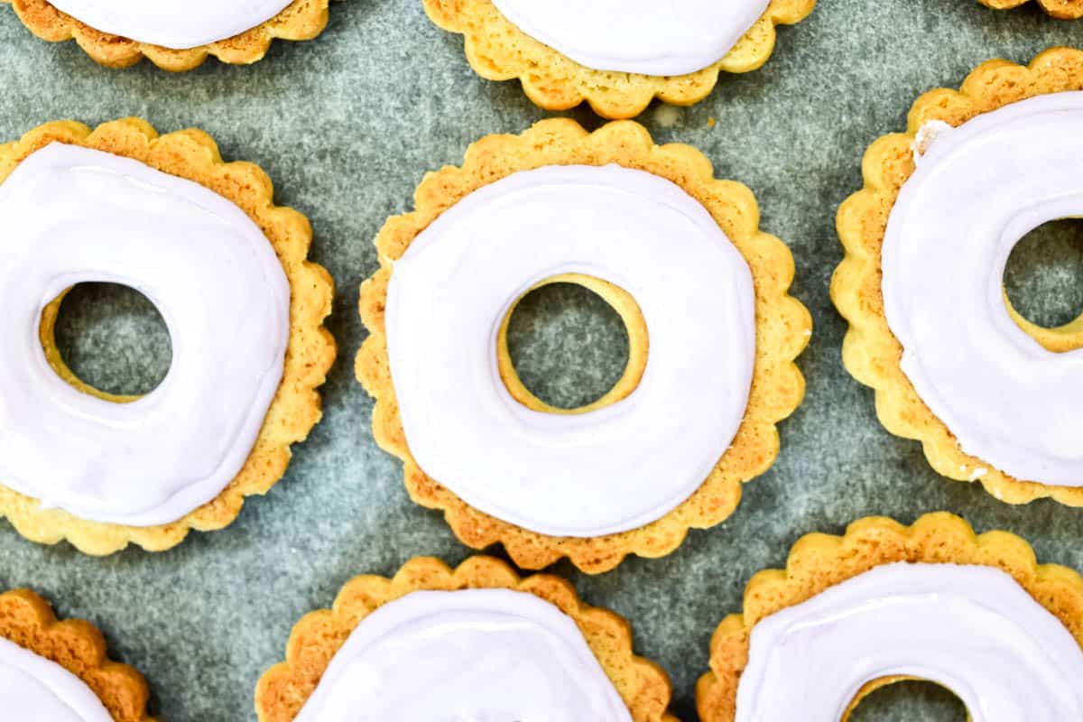 Iced biscuits laid out in rows showing the flood step of flood and line icing.