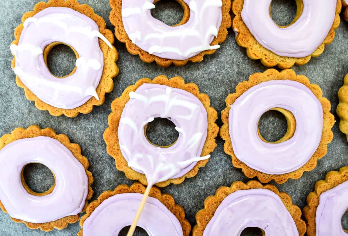 A toothpick is being used to drag white icing in a pattern across the top of the party rings biscuits.