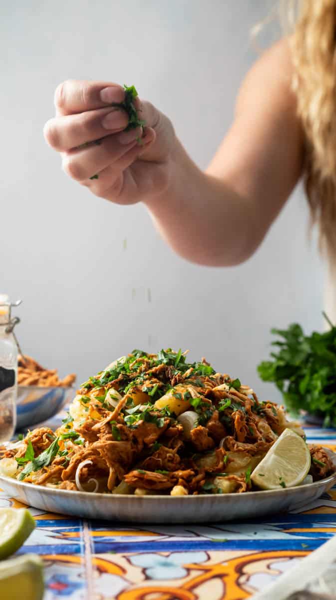 A person is sprinkling fresh parsley on a plate of peri-peri fries.