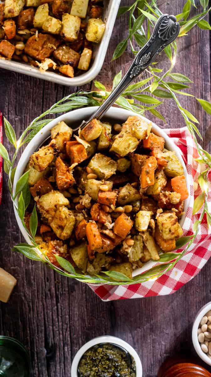 An overhead view of the pesto roasted vegetables in a white bowl with a red napkin wrapped around it. There is a spoon sitting in the bowl.