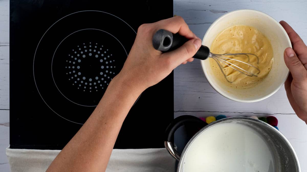 A hand is whisking the ingredients of pastry cream together.