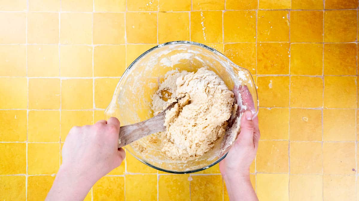 A hand is using a wooden spoon to mix the scone dough together