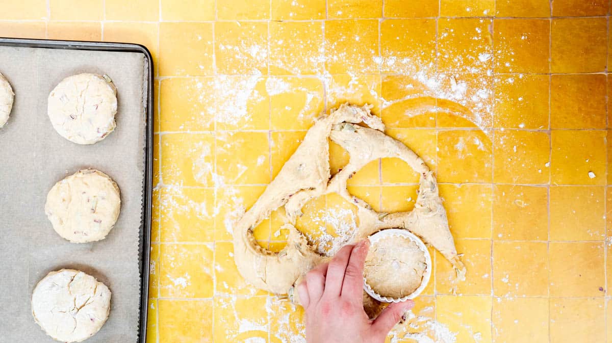A hand this using a cookie cutter to cut rounds of scone dough.