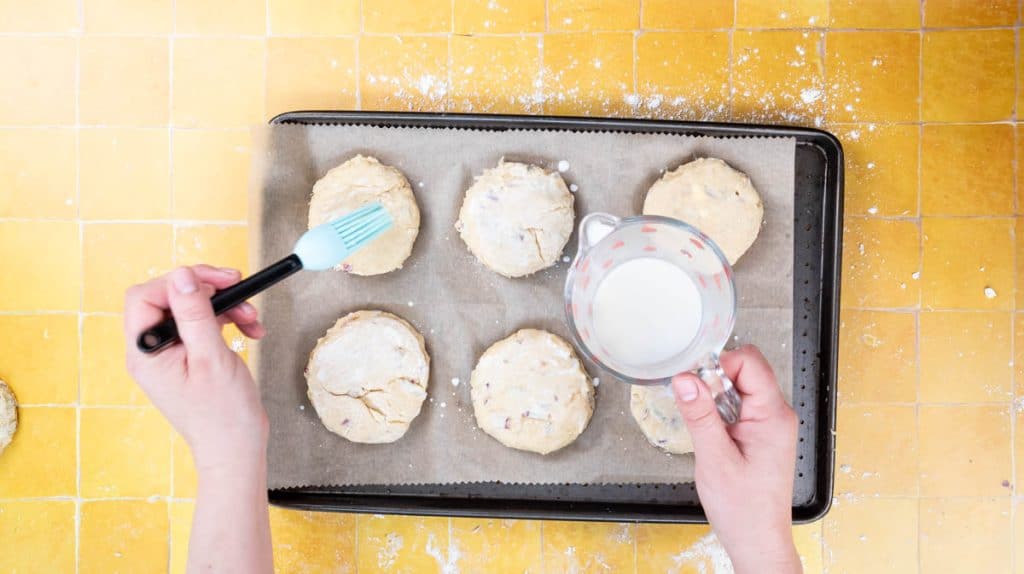 A hand is using a pastry brush to brush the top of the scones with milk.