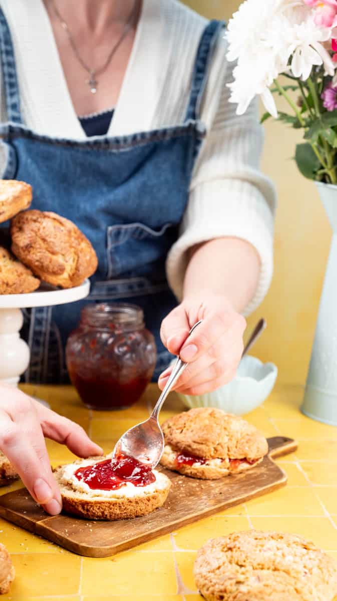 A person is spreading jam onto a sliced rhubarb scone/