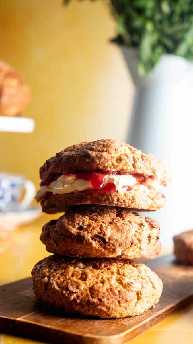 A stack of three rhubarb and ginger scones. The top one is filled with clotted cream and jam.