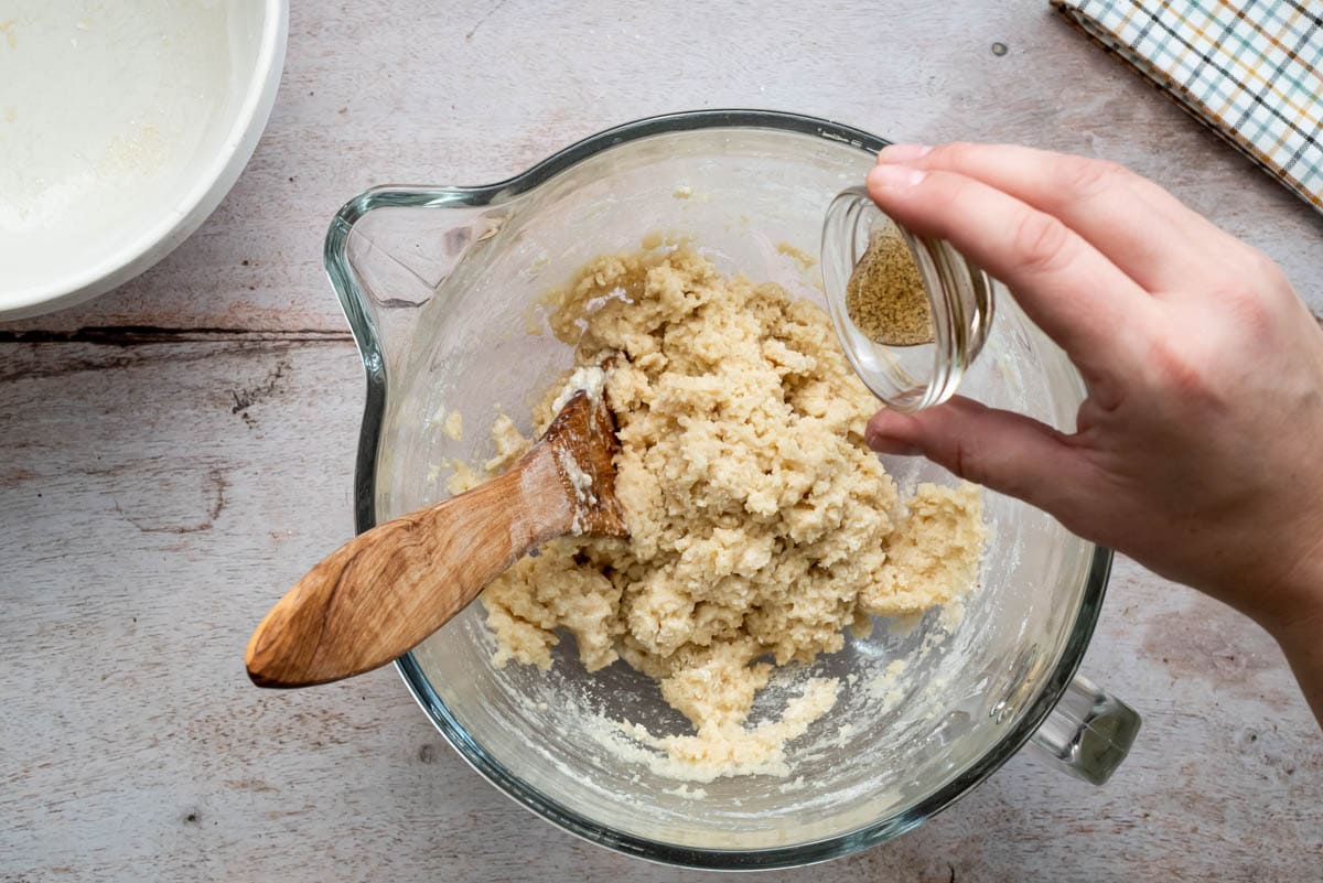 A hand is tipping vanilla extract into the dough ingredients.