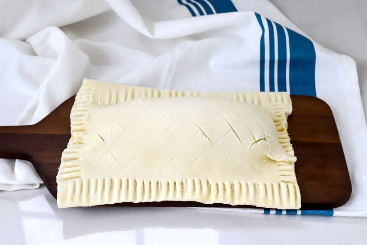 An unbaked salmon puff pastry parcel on a wooden board.