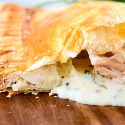 A close-up of a salmon parcel with the dill sauce pouring out onto a wooden board.