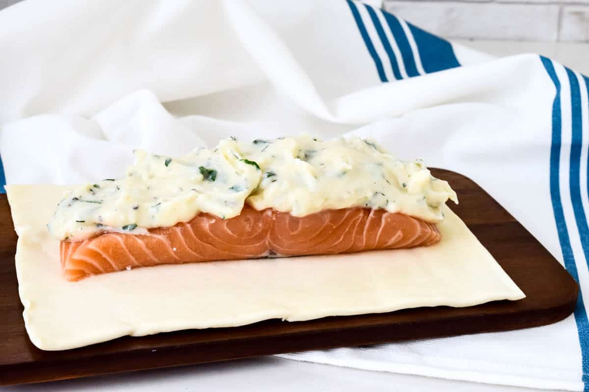 A salmon fillet, topped with dill sauce on a puff pastry sheet.