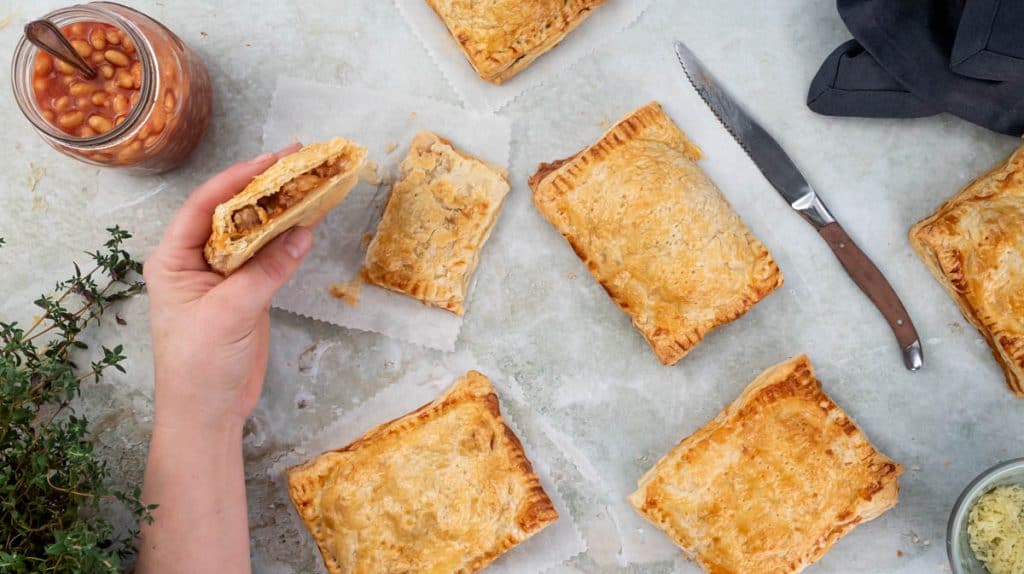 A hand is holding a sliced sausage bean and cheese melt up to show the filling.