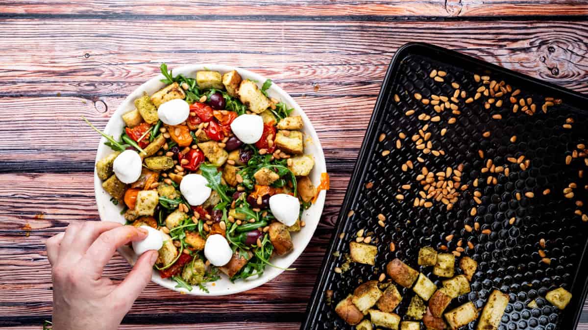 A hand is placing mozzarella pearls into the stale bread salad.