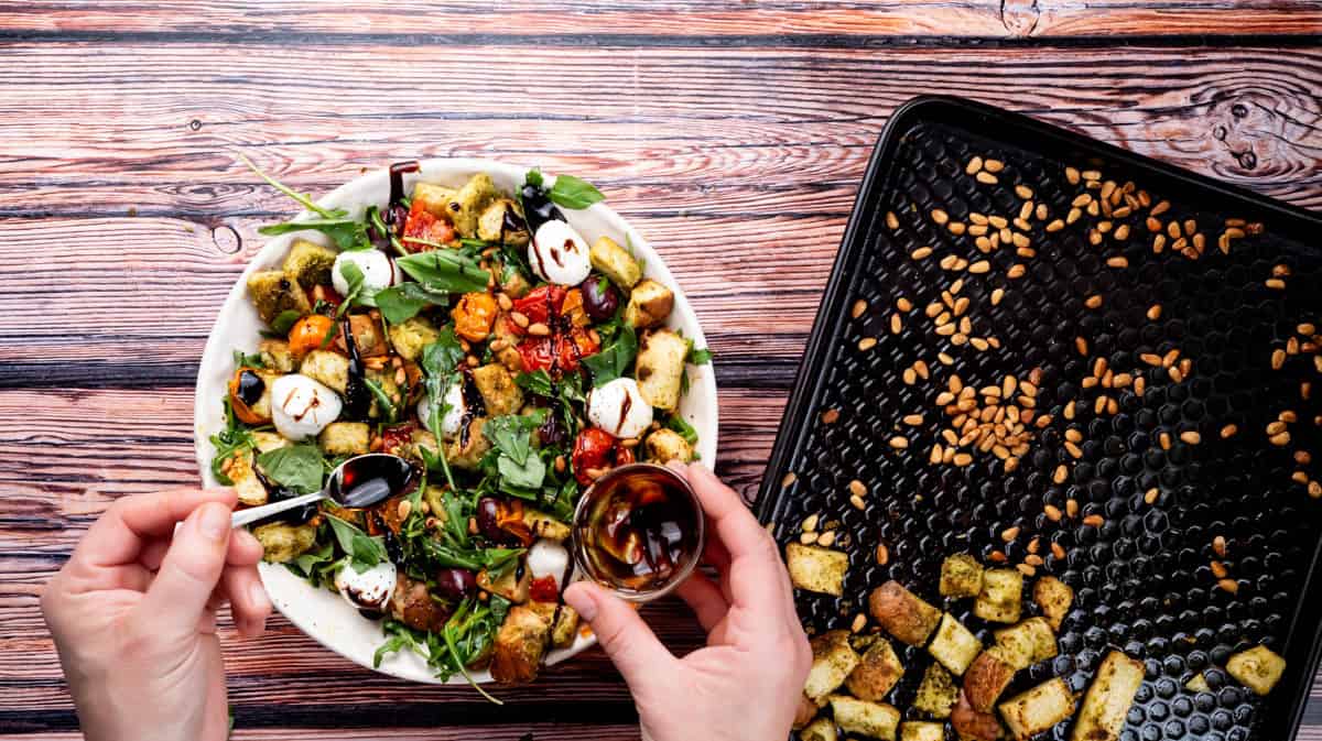 A hand is using a small spoon to drizzle balsamic glaze over the finished stale bread salad.