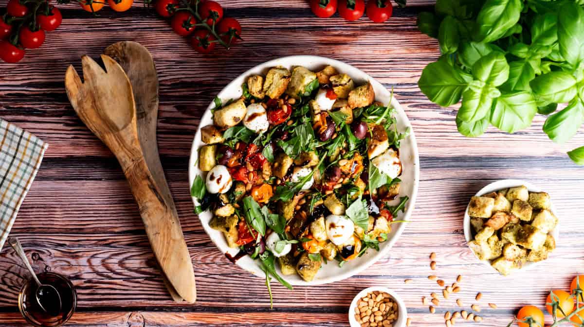A bowl overhead of stale bread salad surrounded by salad tongs and ingredients.