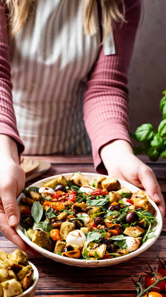 A person is placing a bowl of stale bread salad onto a table.