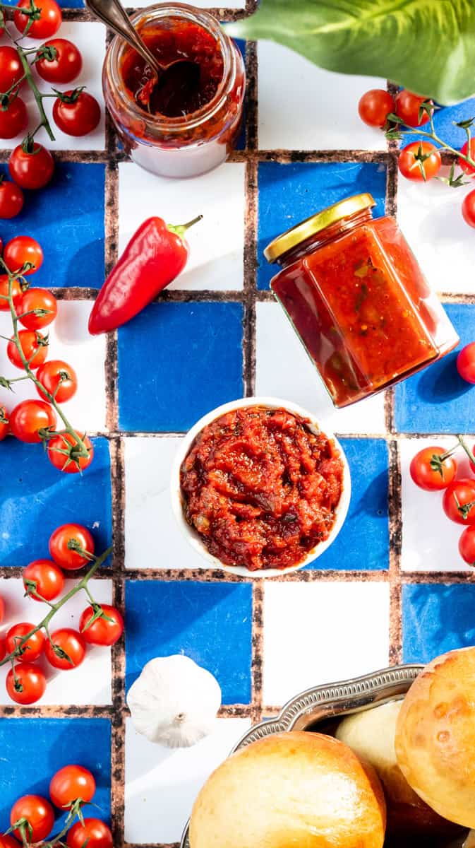 Overhead view of a bowl of tomato burger relish surrounded by ingredients and a jar of relish next to it.