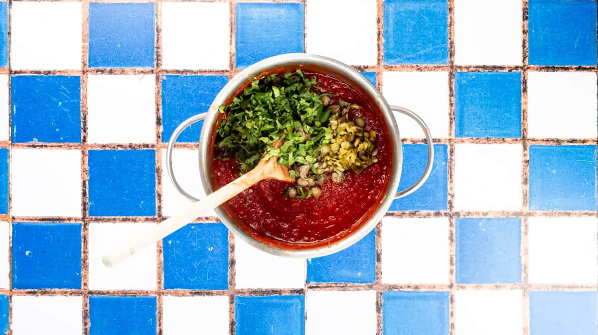 A saucepan with the burger relish with capers, gherkins and chopped coriander on top.