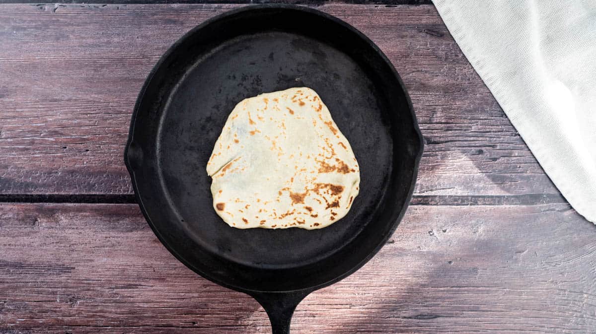 An overhead view of the cast iron pan with the tortilla wrap having been turned over to bake the other side.